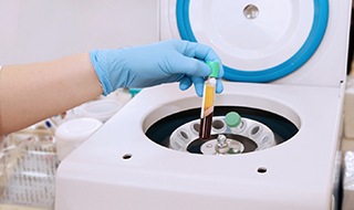 Gloved hand holding vial of processed blood near centrifuge
