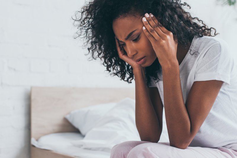 a woman sitting on the side of her bed and experiencing a migraine